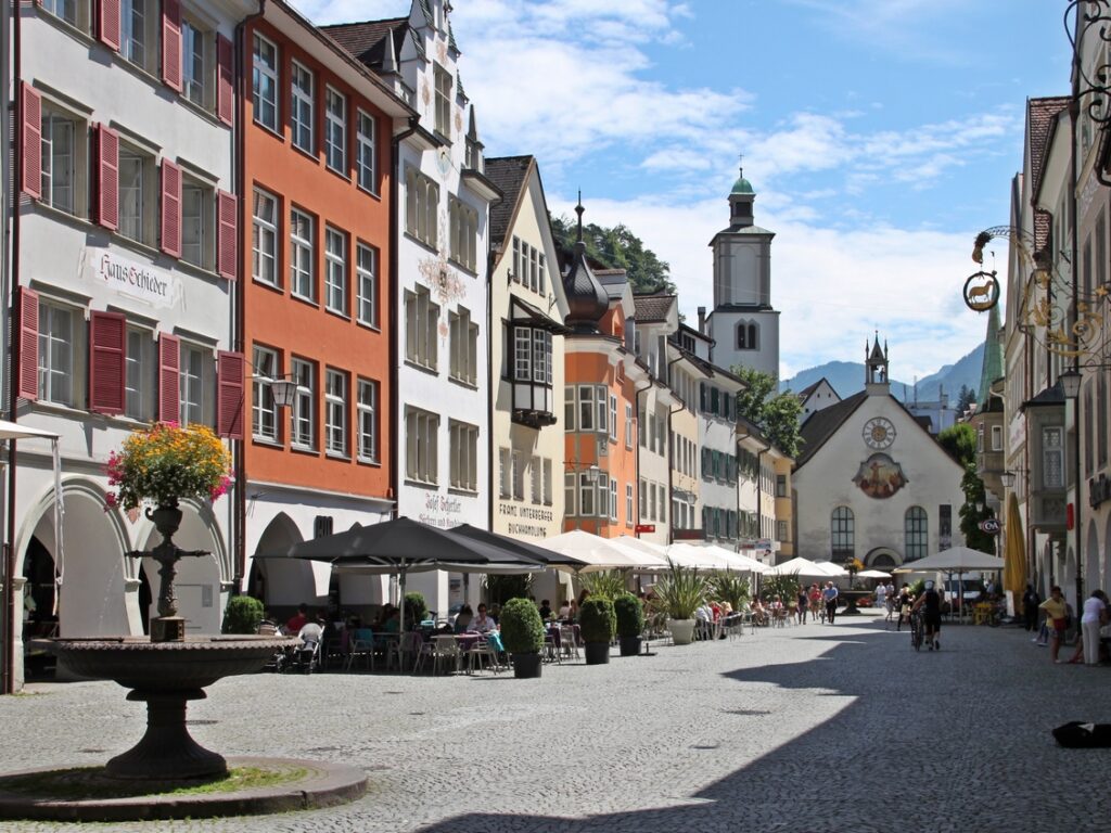 Eine Straße mit pittoresken mittelalterlichen Gebäuden, einem Springbrunnen und einer Kirche.